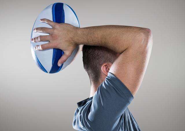 This image shows a man from the side holding a rugby ball above his head, preparing to throw. Ideal for use in sports-related content, articles about rugby, athletic training materials, or promotional materials for rugby events.