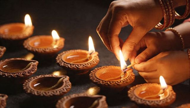 Woman lighting terracotta diyas for diwali celebration, hands with bangles igniting oil lamps