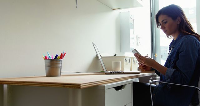 Woman working on laptop and using smartphone in bright home office - Download Free Stock Images Pikwizard.com