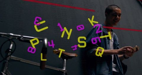 Smiling man holding smartphone beside bicycle with neon letter projection on dark wall