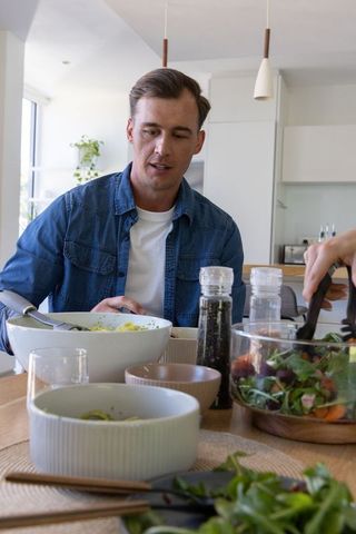 Modern couple enjoying healthy salad at bright kitchen dining table with natural light