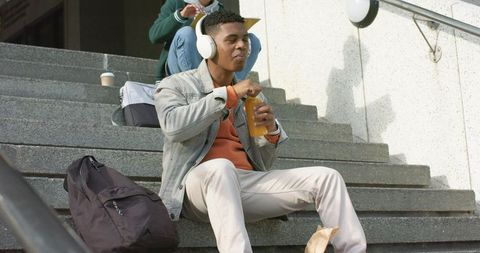 African american college student sitting on campus steps listening to music opening bottle