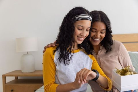 Multiracial mother and teen daughter celebrating with smartwatch gift and warm embrace