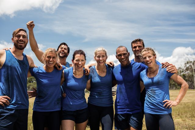 Group of fit individuals posing together in a boot camp setting on a sunny day. They are smiling and showing camaraderie, wearing sportswear. Ideal for use in fitness, teamwork, and outdoor activity promotions, as well as healthy living campaigns.
