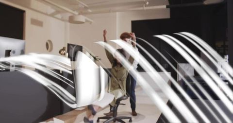 Team celebrating, colleague pushing coworker on swivel chair in modern office