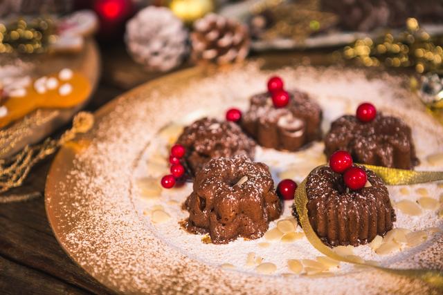 Mini chocolate bundt cakes topped with icing sugar and red berries on a decorative plate. Ideal for holiday baking themes, festive dessert presentations, and Christmas or winter-themed food photography. Perfect for use in recipe blogs, holiday greeting cards, and culinary magazines.