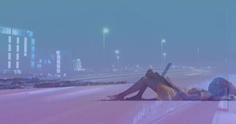Reclining woman on highway at night using laptop with neon light trails and city skyline