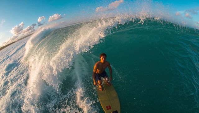 Surfer riding teal barrel on yellow surfboard at reef break during golden hour