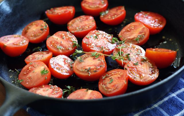 Fresh cherry tomatoes halved and arranged in a cast iron pan with sprigs of herbs, ready for cooking. Ideal for use in culinary blogs, recipe books, or healthy eating articles to emphasize home cooking and fresh ingredients.