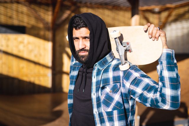 Portrait of biracial man in skateboard shop holding skateboard. Global sport and skateboard shop concept.