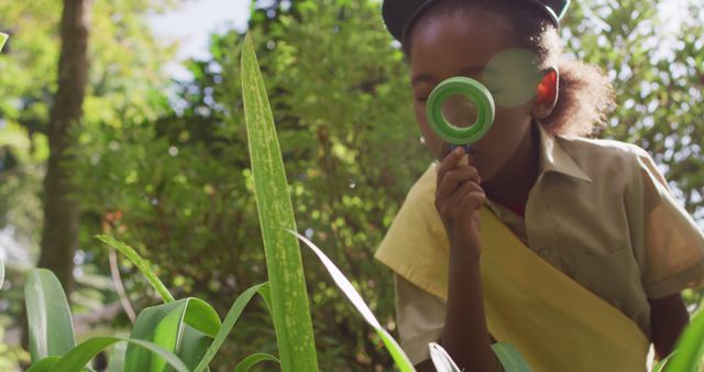 African american girl in scout costume looking at plants with magnifier. childhood, hobby and scouting concept.
