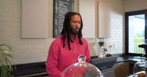 African american barista using touchscreen register behind coffee counter with pastry display