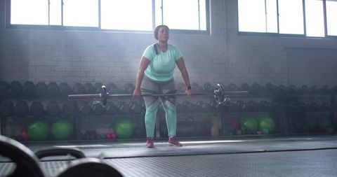 African american woman lifting loaded barbell during strength training in industrial gym