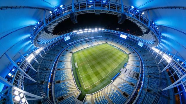 Fisheye view showing modern covered stadium illuminating soccer pitch under blue lights