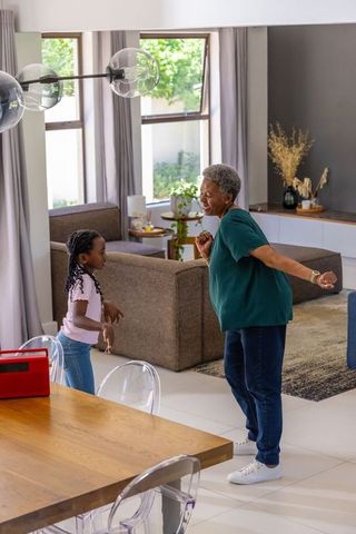 African american grandmother and granddaughter dancing together in bright living room