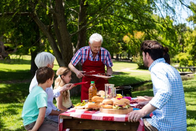 Senior Man Serving Barbeque to Family in Park on Sunny Day - Download Free Stock Photos Pikwizard.com