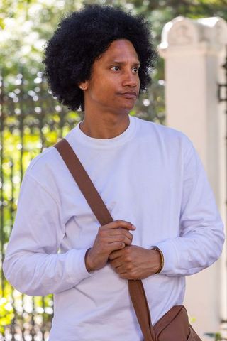 African american man wearing white sweatshirt carrying brown crossbody bag in sunlit park