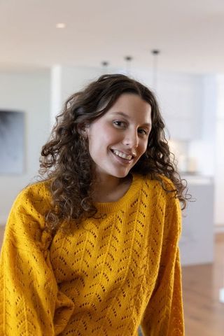 Smiling woman wearing mustard knit sweater leaning on kitchen island cozy curly hair lifestyle portr
