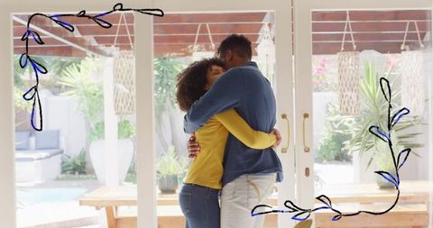 Couple hugging by large glass doors on sunny backyard patio with pool, lanterns, greenery