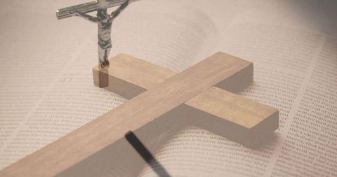 Wooden latin cross casting shadow on open bible with metal crucifix, sepia still life