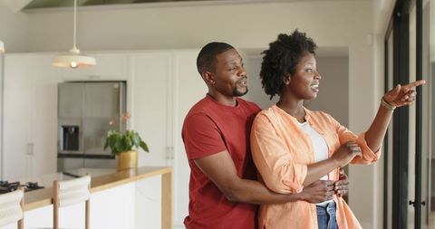 African American Couple Standing in Modern Kitchen, Woman Pointing, Partner Embracing