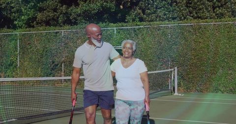 Mature couple enjoying tennis court walk with rackets