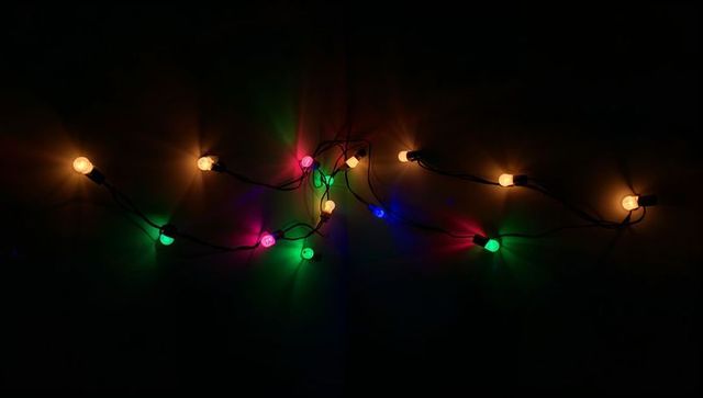 Glowing multicolor festoon lights tangling on dark wall with warm round bulbs and clips