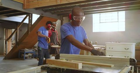 Focused african american woodworkers cutting wooden planks in workshop
