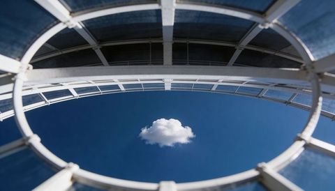 Circular skylight framing single cloud over deep blue sky, geometric glass dome minimalist