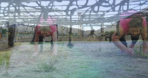 Women crawling under rope net in adventure obstacle course