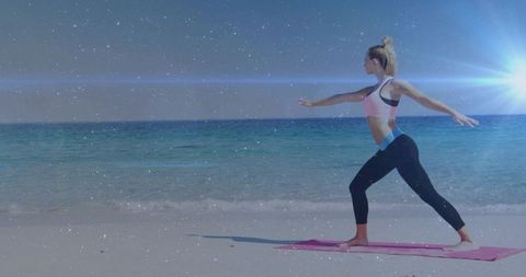Practicing warrior ii on sunny shoreline, woman holding standing yoga pose on pink mat