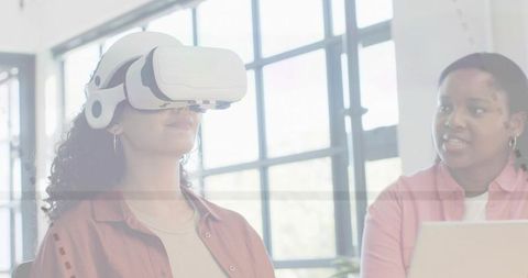 Woman Experiencing VR Training while Colleague Guiding with Laptop in Bright Modern Office