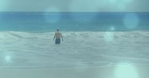 Senior man wading waist-deep into tranquil ocean with breaking waves and soft bokeh
