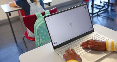 Diverse female students typing on laptop in classroom with mint polka-dot backpack at desks