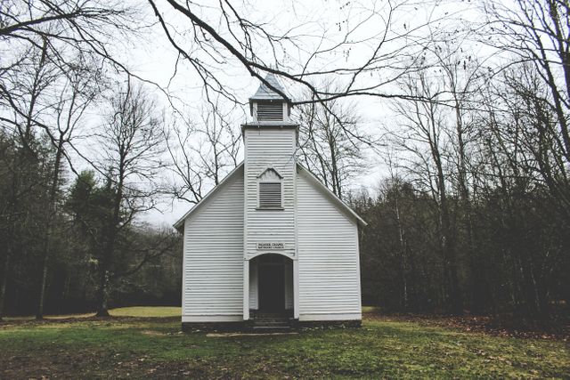 Historic white chapel located in a serene, forested rural area under an overcast sky. Perfect for use in travel brochures, history-related content, religious themed projects, and architecture portfolios highlighting rustic beauty.