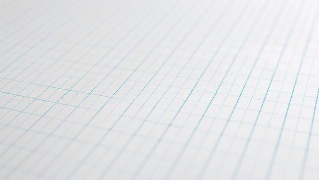 Diagonal close-up featuring blue grid graph paper on desk for design and stationery backgrounds