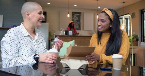 Two diverse women enjoying coffee and cupcakes at cozy modern coffeehouse meetup
