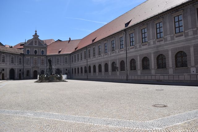 Depiction of an empty courtyard in a historical European building with statues and cobblestone ground. Clear blue sky enhancing the beauty of the historical architecture. Perfect for travel guides, historical sites promotion, architectural studies, and educational materials.