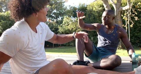 Friends chatting and hydrating on sunny backyard deck after outdoor workout session