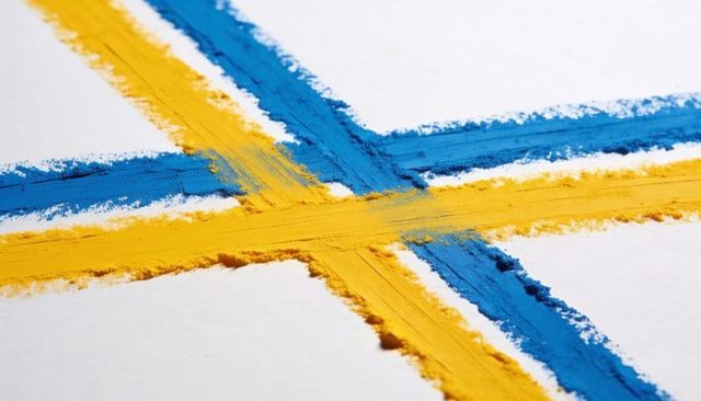 Vibrant blue and yellow pigment cross on textured paper with dramatic brush strokes