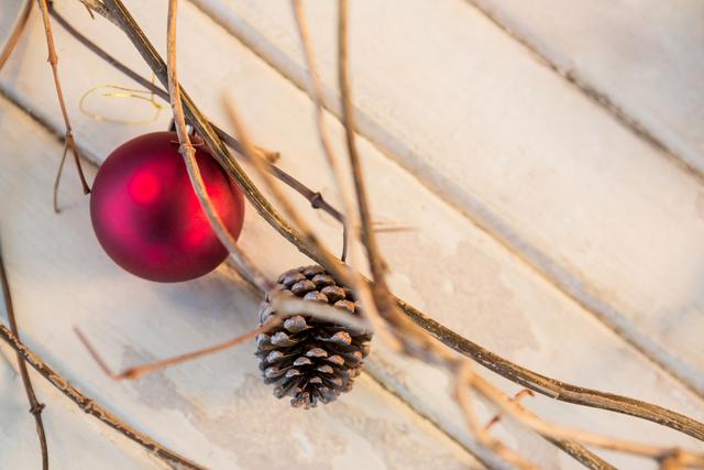 This image captures a red Christmas bauble and a pine cone hanging on branches over a rustic wooden plank. Ideal for holiday greeting cards, festive blog posts, seasonal marketing materials, and Christmas-themed decorations.