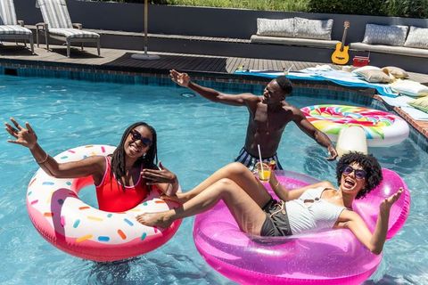 Young friends enjoying backyard pool party on colorful inflatable floats and drinks