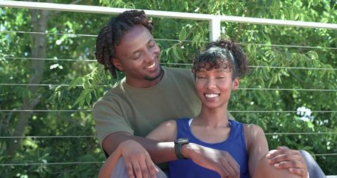 African american couple sitting on balcony smiling and embracing with smartwatch visible