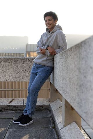 Teen smiling in hoodie leaning on rooftop parapet at golden hour urban casual vibe