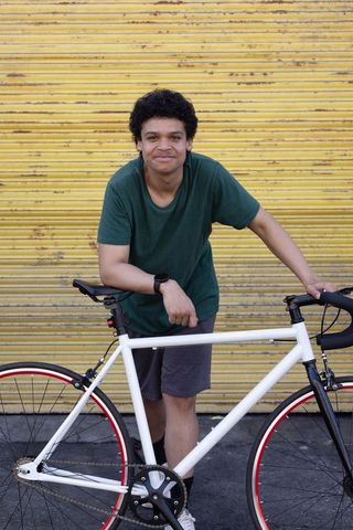 African american man leaning on white road bike wearing smartwatch against yellow backdrop
