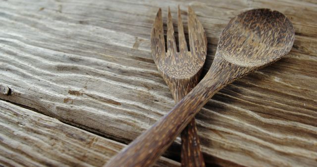 This image showcases a rustic wooden fork and spoon set lying on a textured wooden surface. The natural look of the utensils highlights eco-friendly and handcrafted kitchenware. Ideal for use in articles, blogs, or advertisements focused on sustainable living, organic dining, or rustic interior decor.