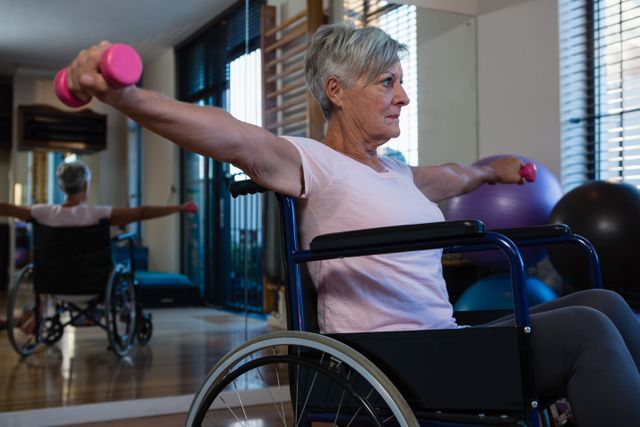 Senior woman in wheelchair lifting dumbbells in a clinic. Ideal for use in articles or advertisements related to physical therapy, rehabilitation, senior fitness, healthcare services, and promoting active lifestyles among the elderly.