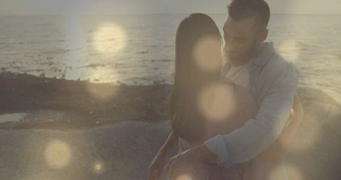Romantic couple embracing on sunlit shoreline with cinematic lens flare at sunset
