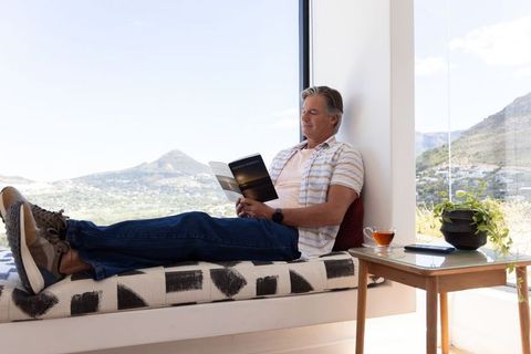Man reclining on window seat reading paperback with panoramic mountain view