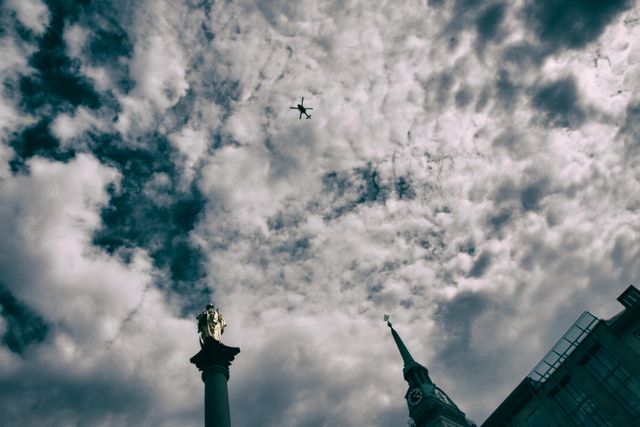 This image captures an airplane flying above a historic cityscape with a prominent statue, steeple, and old architecture under a cloudy sky. Ideal for use in travel and tourism promotions, urban exploration content, and architectural themes.